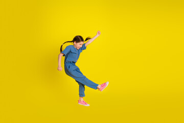 Obraz premium Preteen girl joyfully jumping in a stylish blue outfit against a vibrant yellow background, expressing happiness