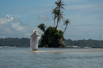 The wind blows the shawl worn by a woman standing on a tropical beach. Happy young woman wearing a shawl on the beach on a sunny day