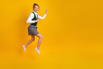 Fototapeta premium Smiling teenage schoolgirl jumping joyfully on yellow background wearing stylish uniform showcasing cheerful youthful energy