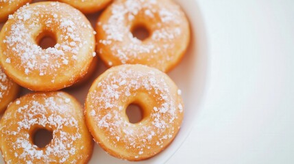 A white plate filled with golden donuts dusted with powdered sugar, with a clean white background and copy space