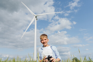 Teen boy with camera standing in wheat field near wind turbine, smiling