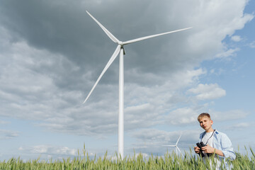 Teen boy holding binoculars in front of tall wind turbine, cloudy sky