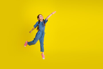 Obraz premium Happy young girl enjoying playful jump in vibrant yellow background wearing stylish blue jumpsuit and pink sandals