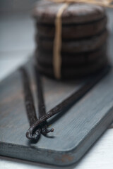 Close up studio still life photo with soft light and muted colors featuring dried vanilla beans on a vintage wooden board  with espresso and cookies in the background