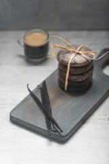 Close up studio still life photo with soft light and muted colors featuring dried vanilla beans on a vintage wooden board  with espresso and cookies in the background