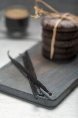 Close up studio still life photo with soft light and muted colors featuring dried vanilla beans on a vintage wooden board  with espresso and cookies in the background, 