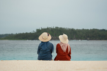Two friends enjoy the beauty of Indonesia's tropical beaches. Two young women sit together and chat on a beautiful tropical beach