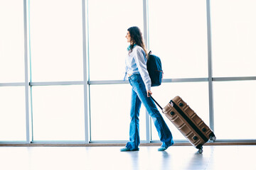 Young woman casually walking with luggage in an airport terminal on a sunny day, reflecting tourism...