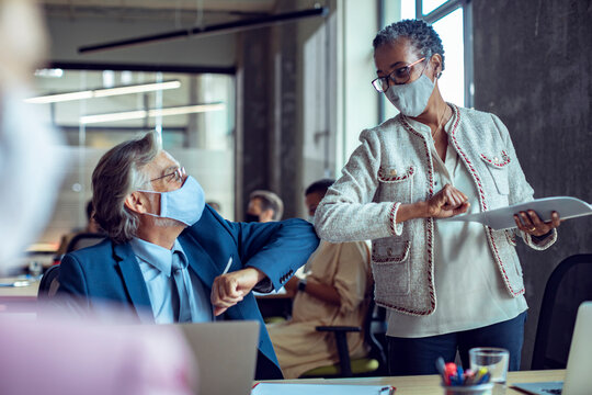 Coworkers greeting with elbow bump in office while wearing masks