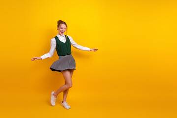 Happy teen schoolgirl posing playfully in uniform against bright yellow background, showcasing...