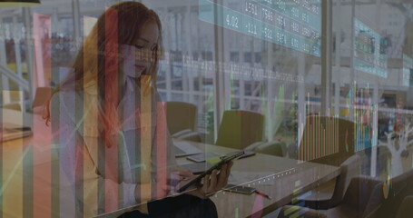 Holding tablet and stylus pen, woman wearing dotted blouse studying financial charts in open office