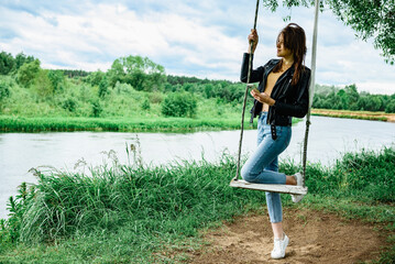 A happy young girl is standing on a swing in a beautiful tree by the river.