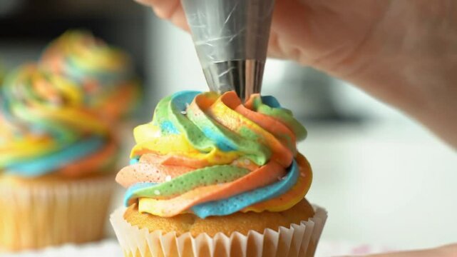 Close up of a person decorating a cupcake with colorful frosting using a piping bag tool