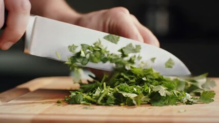 Close up of hands chopping fresh parsley with a large silver knife on a wooden cutting board - Powered by Adobe