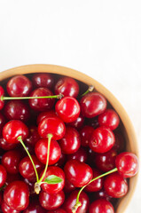 Ripe red cherries in a wooden bowl on a white background. Concept of summer berry harvest. Vertical orientation. Selective focus. Top view. Copy space.