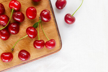 Ripe red cherries on a wooden cutting board on a white background. Concept of summer berry harvest. Horizontal orientation. Selective focus. Top view. Copy space.