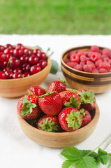 Three types of berries in ceramic bowls on a white background. Strawberries, cherries and raspberries. Summer berry harvest concept. Vertical orientation. Selective focus.