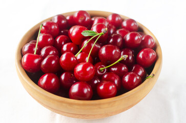 Ripe red cherries in a ceramic bowl on a white background. Concept of summer berry harvest. Horizontal orientation. Selective focus.