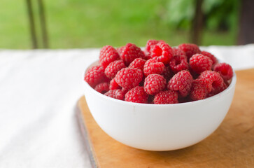 Ripe pink raspberries in a bowl on a white background. Concept of summer berry harvest. Horizontal...