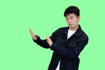 young asian man making rejection or dissaproval pose in green isolated background