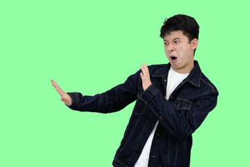 young asian man making rejection or dissaproval pose in green isolated background
