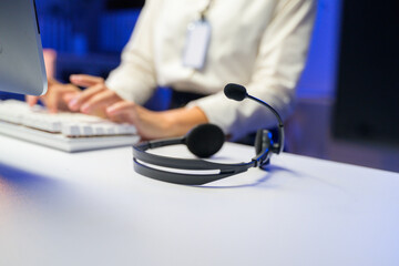 Headset lying on desk while female call center operator is working in blurred background