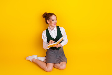 Young student on a bright yellow background holding a book while expressing joy and an academic...