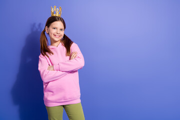 Charming young girl in casual hoodie poses confidently with a crown accessory against a vibrant...