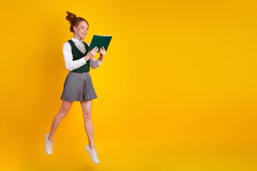 Joyful teenager enthusiastically reading a book while jumping high on a bright yellow background
