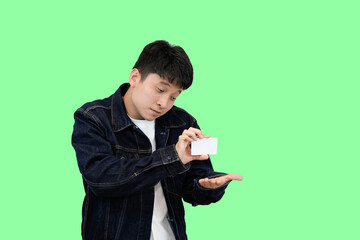 young asian man showing credit card in green isolated background
