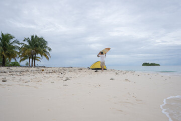 Aerial view of a surfer walks on a beautiful tropical beach carrying a surfboard. A male surfer walks alone on the beach