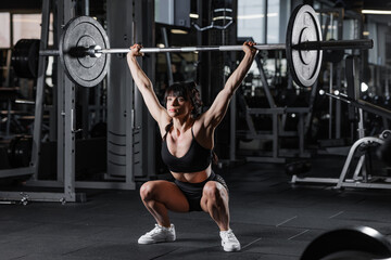 Strong fit woman performing overhead squat with barbell in gym strength training workout sports...