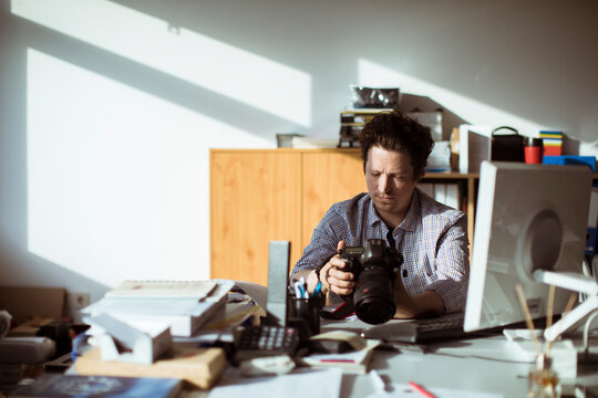 Male photographer reviewing camera in creative office workspace