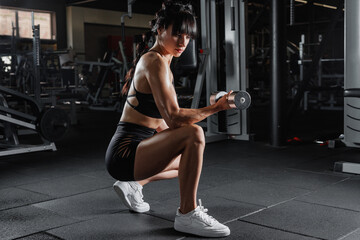 Fit woman squatting with dumbbell in gym showing strength motivation and real workout training