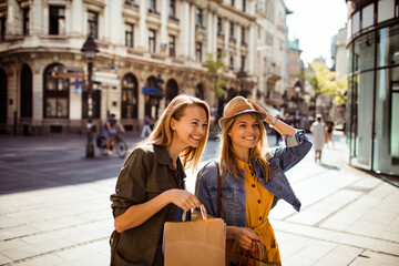 Two happy women shopping and laughing together in city on sunny day