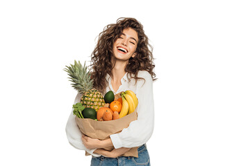 Happy woman holding a grocery bag full of fresh fruits.