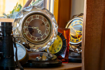collection of vintage alarm clocks and table clocks on a wooden windowsill. Warm daylight and glass...