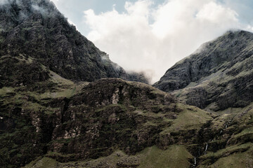 Fog drifts over rocky, green terrain leading up to the peak of Carrauntoohill in County Kerry,...