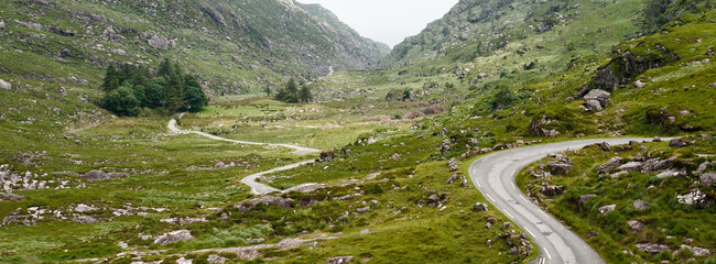 Emerald hillsides embrace a narrow asphalt road, creating a mesmerizing journey through Ireland's...