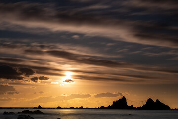 神奈川県真鶴町の名勝・真鶴岬三ツ石に昇る朝日。オレンジ色の朝焼けと波打つ岩礁海岸が幻想的な絶景を創出。冬の澄んだ空気と静寂に包まれた神秘的な景色は、旅行・観光・自然風景・パワースポットのイメージに最適です。

