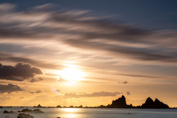 神奈川県真鶴町の名勝・真鶴岬三ツ石に昇る朝日。オレンジ色の朝焼けと波打つ岩礁海岸が幻想的な絶景を創出。冬の澄んだ空気と静寂に包まれた神秘的な景色は、旅行・観光・自然風景・パワースポットのイメージに最適です。

