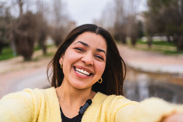 Young influencer smiling and creating content for social media, recording a video with a lavalier microphone in a park
