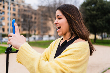 Young woman vlogger recording video for social media with her phone on a tripod in a park