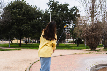 Young woman vlogging in a park using a selfie stick and smartphone