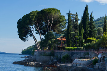A beautiful seaside villa with a terracotta roof, surrounded by lush green trees and cypress trees,...