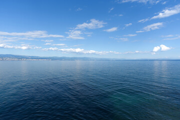 A tranquil blue sea stretches under a vast sky dotted with white clouds, with a distant coastline visible on the horizon.