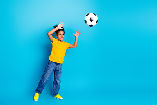 Smiling young girl playing with a soccer ball against a vibrant blue background, exuding fun, joy, and charm - Powered by Adobe