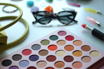 Green bag, various colorful jewelry, sunglasses, hair accessories and colorful make up on white background. Selective focus.