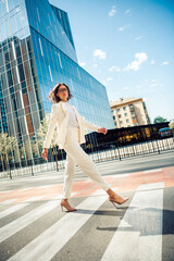 Elegant professional businesswoman in white suit walking confidently outdoors in urban city...