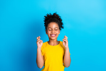 Bright cheerful girl with fingers crossed excitingly on a blue background expressing hope and happiness